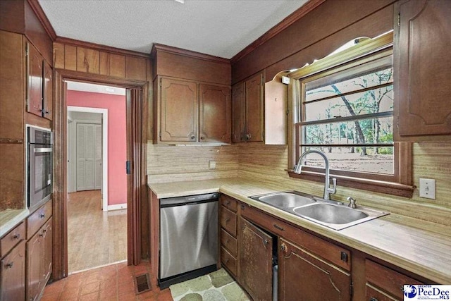 kitchen featuring stainless steel appliances, a sink, light countertops, decorative backsplash, and crown molding