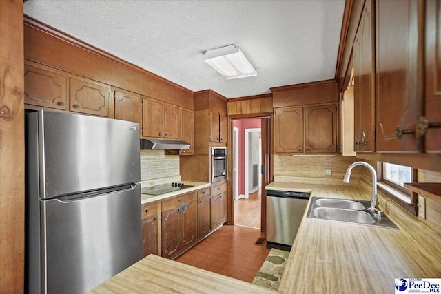 kitchen featuring light countertops, appliances with stainless steel finishes, brown cabinetry, a sink, and under cabinet range hood