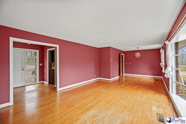 empty room with a chandelier, plenty of natural light, and light wood-style floors