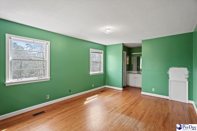 unfurnished bedroom with a textured ceiling, ensuite bathroom, wood finished floors, visible vents, and baseboards