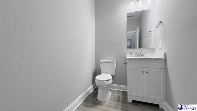 half bathroom featuring toilet, visible vents, baseboards, wood finished floors, and vanity