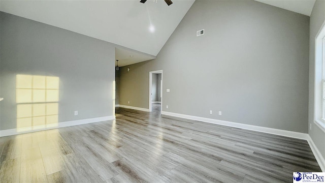 unfurnished room featuring wood finished floors, visible vents, a ceiling fan, baseboards, and high vaulted ceiling