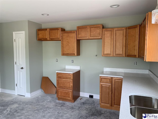 kitchen with recessed lighting, a sink, brown cabinetry, light carpet, and baseboards