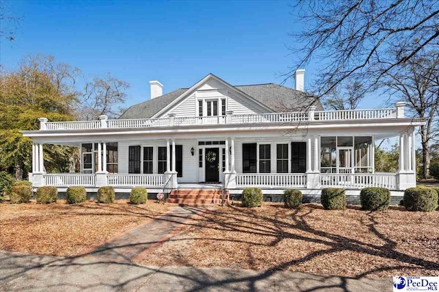 view of front facade with covered porch, a chimney, and a sunroom