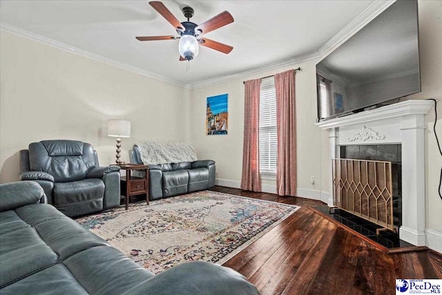 living room featuring crown molding, dark wood finished floors, a tiled fireplace, a ceiling fan, and baseboards