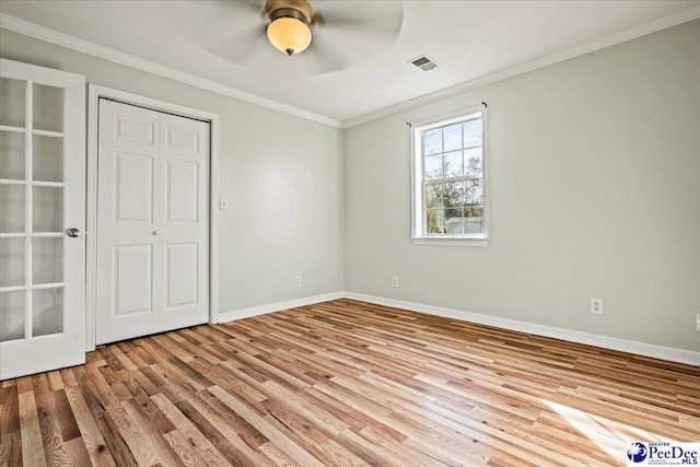 unfurnished bedroom featuring crown molding, visible vents, a ceiling fan, wood finished floors, and baseboards