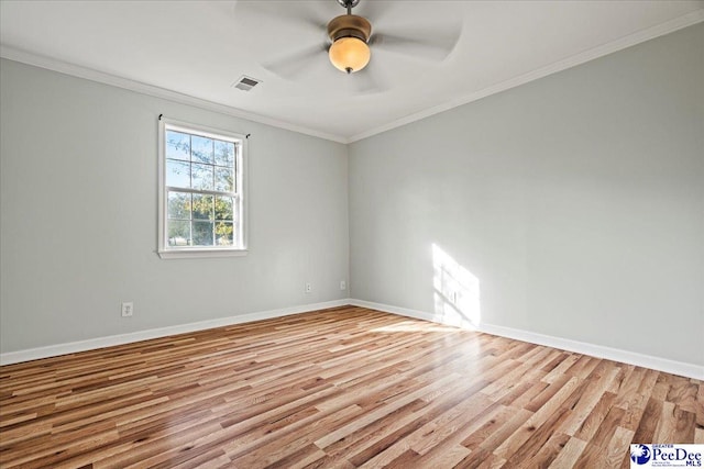 empty room with baseboards, wood finished floors, visible vents, and crown molding