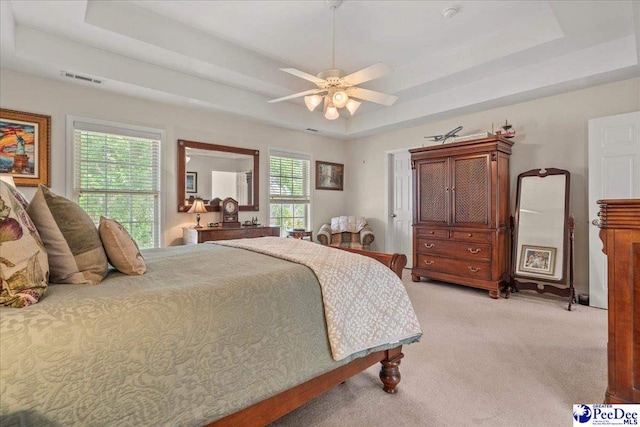 bedroom with a raised ceiling, light carpet, and ceiling fan