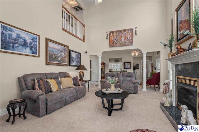 carpeted living room with ornate columns, a high ceiling, a fireplace, and baseboards