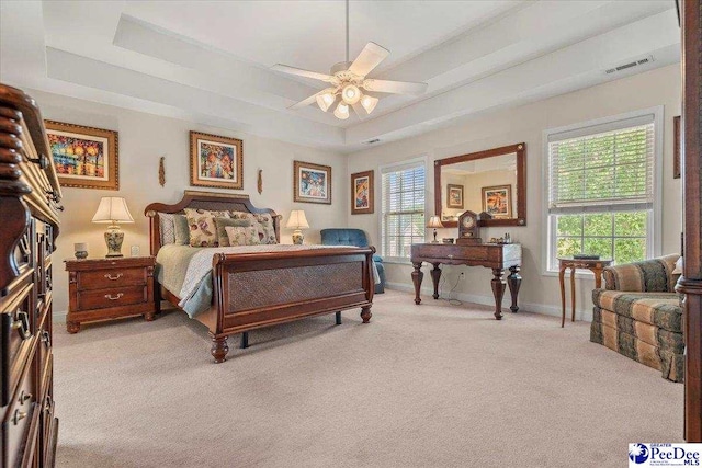 bedroom with light colored carpet, a tray ceiling, multiple windows, and baseboards