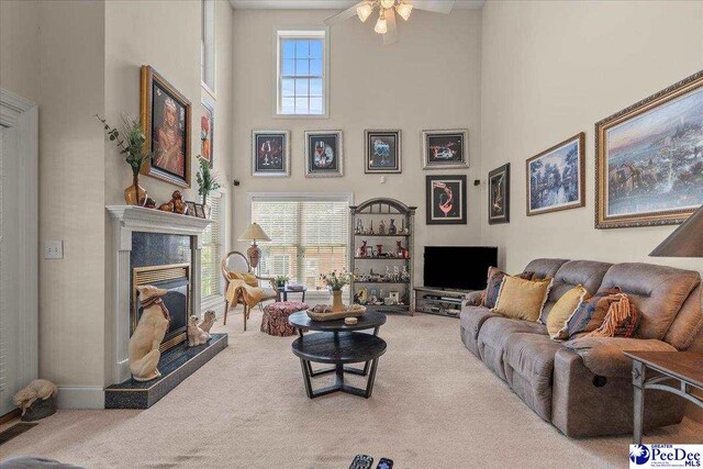 living room with a towering ceiling, carpet floors, a glass covered fireplace, and a ceiling fan
