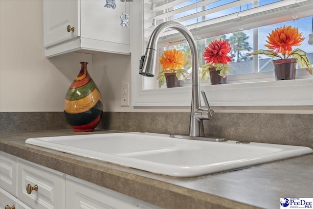 kitchen view of a sink, white cabinetry, and dark countertops