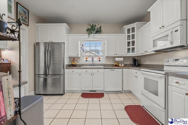 kitchen with white appliances, a sink, white cabinetry, light tile patterned flooring, and dark countertops