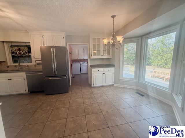 kitchen with appliances with stainless steel finishes, dark countertops, white cabinetry, and a notable chandelier