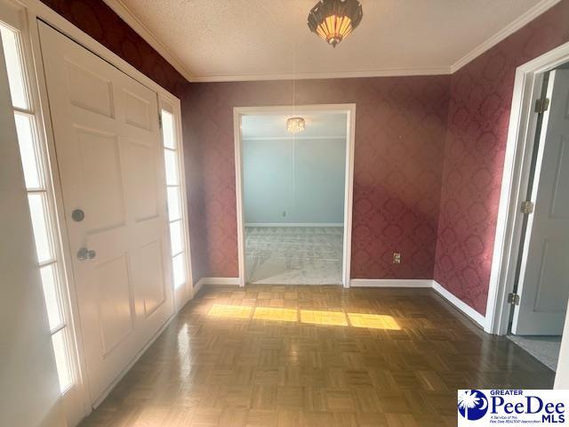 entrance foyer with ornamental molding, a textured ceiling, baseboards, and wallpapered walls