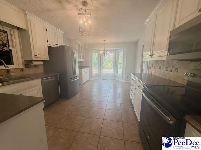 kitchen featuring a sink, white cabinets, appliances with stainless steel finishes, dark countertops, and an inviting chandelier