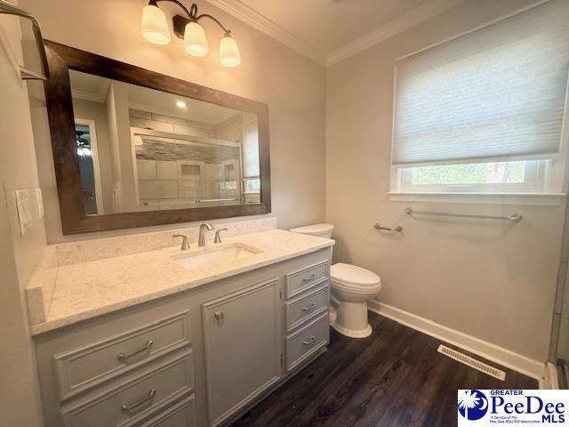 full bathroom with ornamental molding, a tile shower, toilet, and wood finished floors