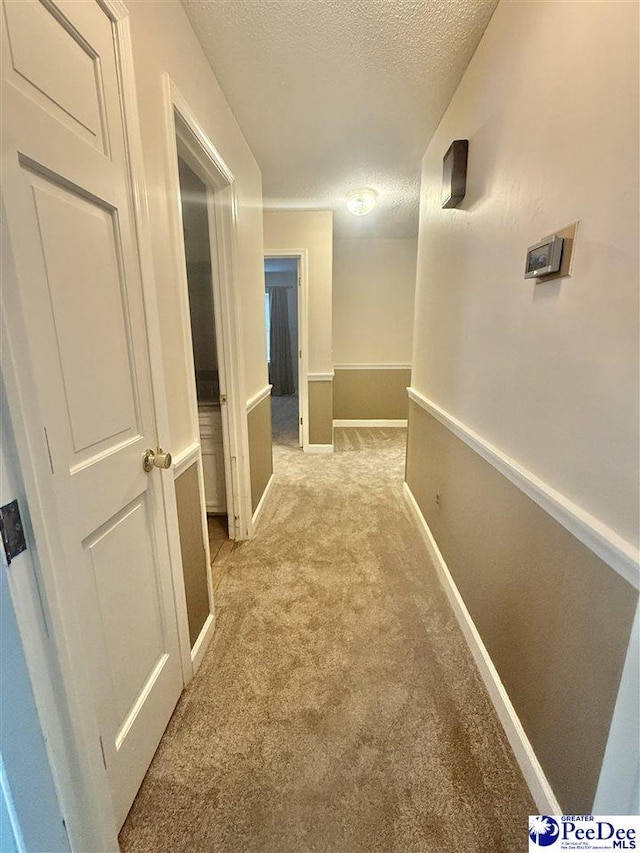 corridor with light carpet, a textured ceiling, and baseboards