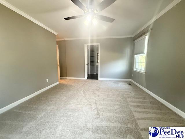 carpeted spare room with baseboards, a ceiling fan, and crown molding