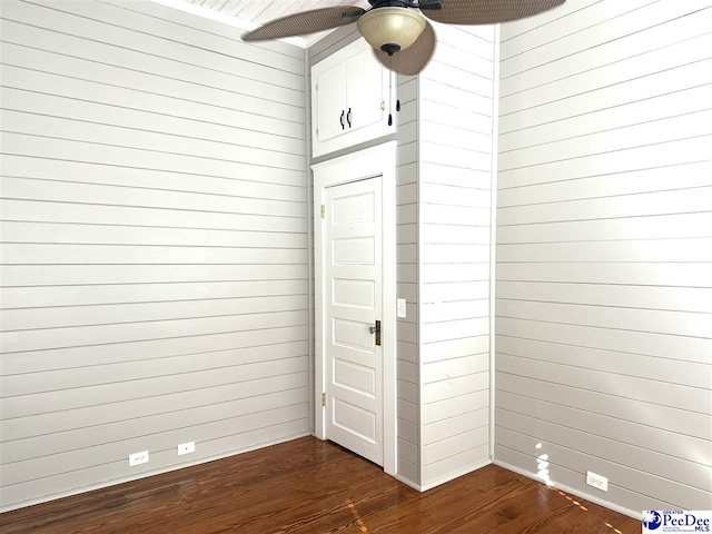 empty room with dark hardwood / wood-style floors, ceiling fan, and wooden walls