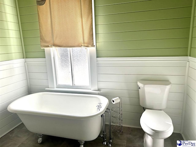 bathroom with toilet, a tub, and wood walls