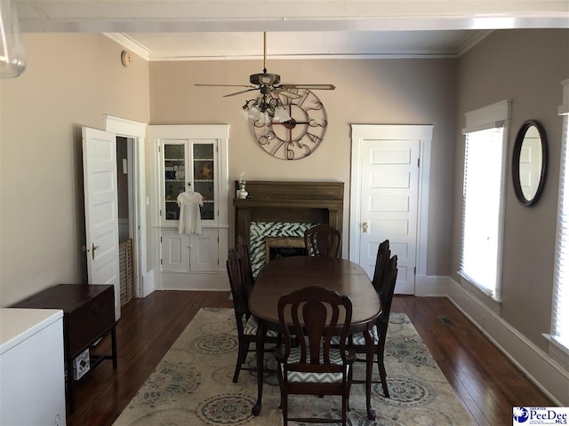 dining area featuring dark wood-type flooring, ornamental molding, a tile fireplace, and ceiling fan