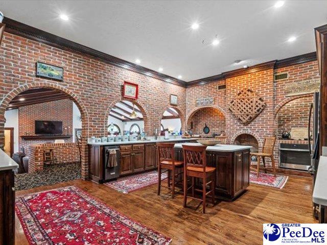 bar with brick wall, ornamental molding, hardwood / wood-style floors, and dark brown cabinets