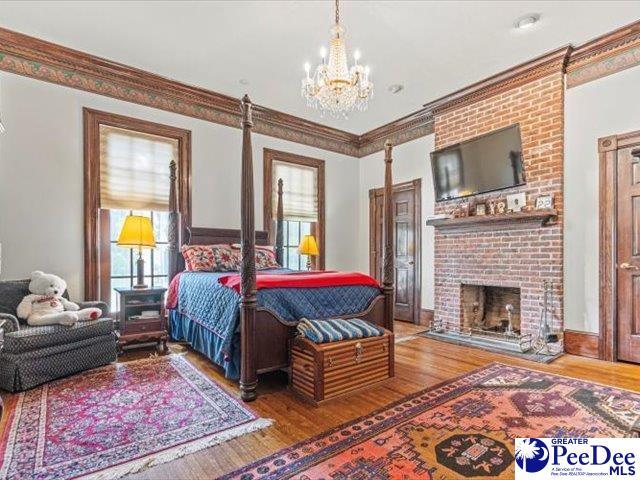 bedroom featuring ornamental molding, a brick fireplace, hardwood / wood-style floors, and an inviting chandelier