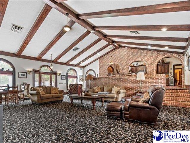 living room featuring brick wall, beam ceiling, high vaulted ceiling, and carpet