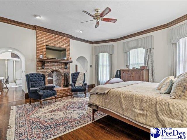 bedroom featuring crown molding, dark wood-type flooring, ceiling fan, and a fireplace