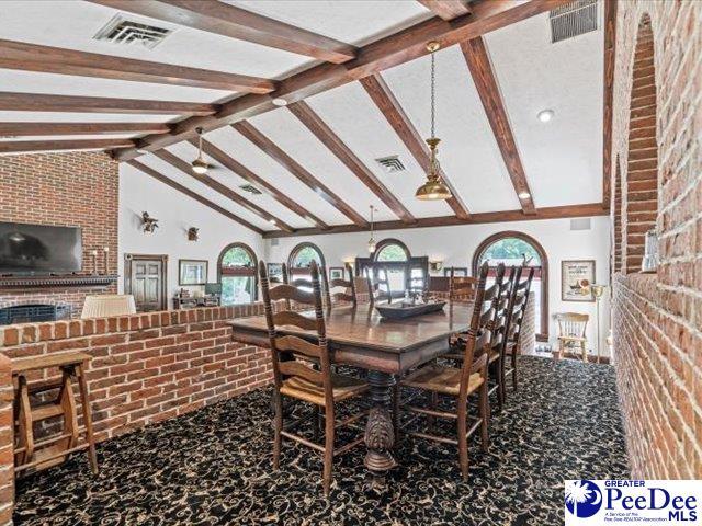 carpeted dining room featuring high vaulted ceiling, beamed ceiling, and brick wall