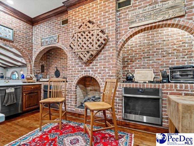 interior space featuring dark wood-type flooring, crown molding, stainless steel oven, dishwasher, and brick wall