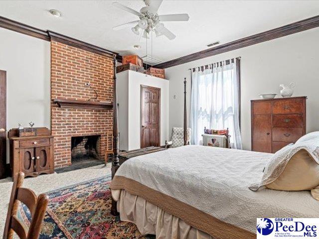 bedroom with crown molding, a brick fireplace, and ceiling fan