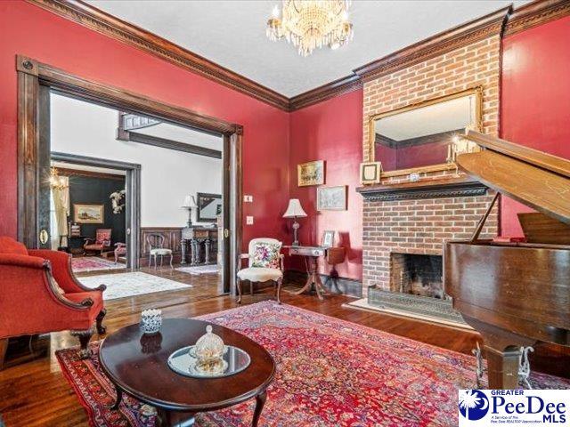 living room featuring an inviting chandelier, wood-type flooring, crown molding, and a brick fireplace