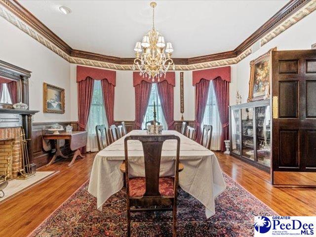 dining area featuring ornamental molding, hardwood / wood-style floors, a brick fireplace, and a notable chandelier