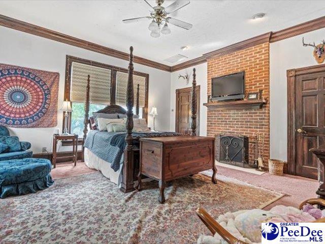 carpeted bedroom featuring ornamental molding, a brick fireplace, and ceiling fan