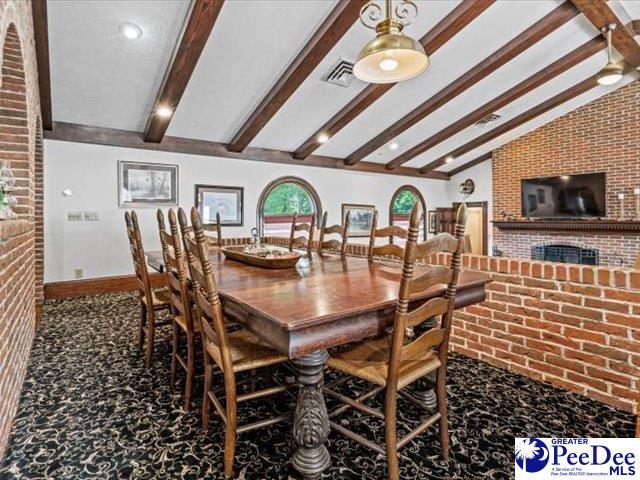 dining space featuring lofted ceiling with beams, brick wall, carpet flooring, and a fireplace