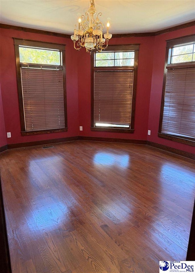 spare room featuring a chandelier, baseboards, and wood finished floors