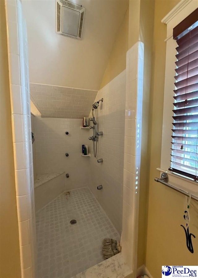 bathroom featuring lofted ceiling, visible vents, and tiled shower