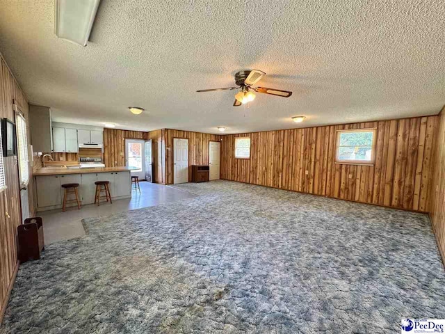 unfurnished living room featuring wood walls, a textured ceiling, a ceiling fan, and a wealth of natural light