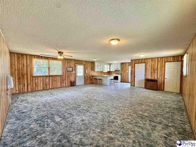 unfurnished living room featuring wood walls, a textured ceiling, a ceiling fan, and carpet flooring