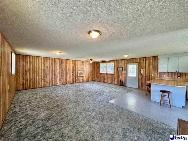 unfurnished living room featuring wood walls, carpet flooring, a wall mounted air conditioner, a textured ceiling, and a ceiling fan