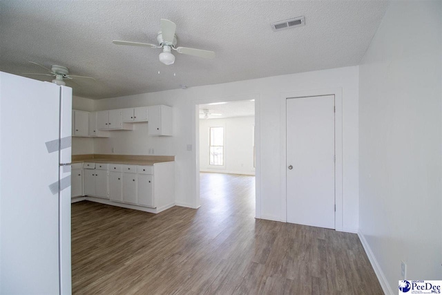 kitchen featuring a textured ceiling, wood finished floors, visible vents, white cabinetry, and freestanding refrigerator