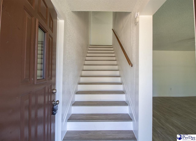 stairway featuring baseboards, wood finished floors, a textured ceiling, and a textured wall