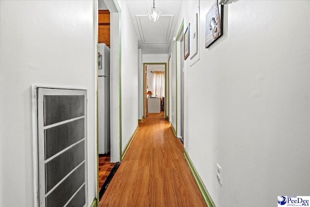 hallway with a heating unit, wood finished floors, and attic access