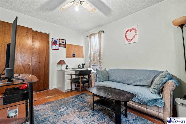 living area with a textured ceiling, a ceiling fan, and wood finished floors