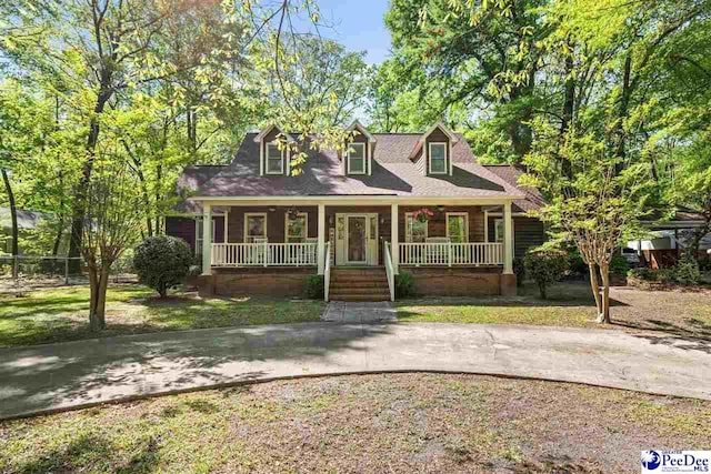 cape cod home featuring a porch and a front lawn
