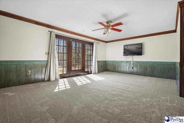 unfurnished living room featuring ceiling fan, carpet flooring, ornamental molding, french doors, and wainscoting