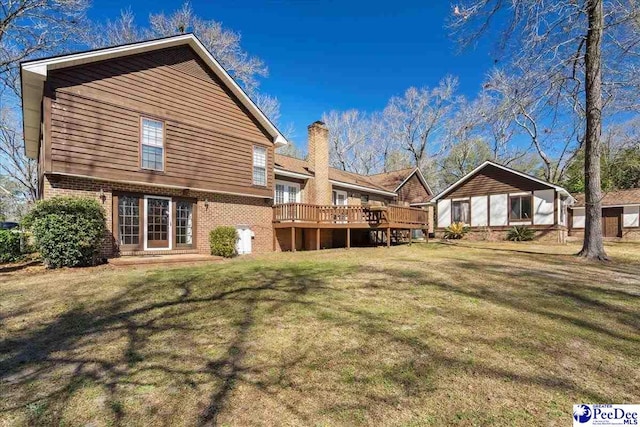 back of house with brick siding, a lawn, a chimney, and a wooden deck