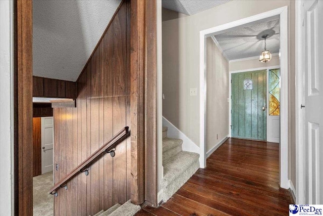 stairway with crown molding, wood walls, a textured ceiling, wood finished floors, and baseboards